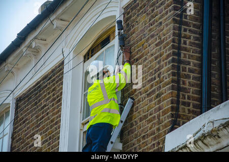 Un ingegnere Openreach su una scala lavorando su una linea telefonica che collega a una proprietà residenziale. Foto Stock