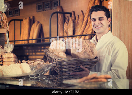 L'uomo vendita di pasticceria e baguette nella panetteria locale Foto Stock