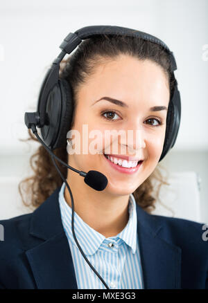 Ritratto di cordiale sorriso attraente giovane donna con cuffia di risposta a una chiamata in ufficio Foto Stock