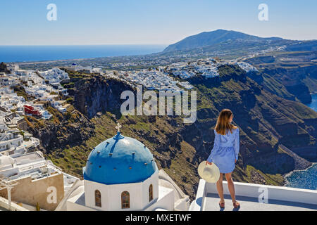 Giovane donna sorge su di una collina e guarda il paesaggio marino di Santorini, Grecia Foto Stock