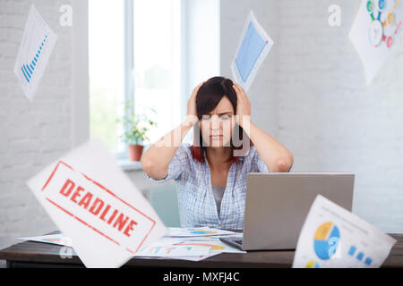 Stanco disturbati lavoratrice con mal di testa e la caduta di carte intorno a. Ha sottolineato la donna in ufficio tenendo la testa nelle mani e pensando a scadenza. Sposta in Foto Stock