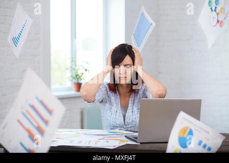 Stanco disturbati lavoratrice con mal di testa e la caduta di carte intorno a. Ha sottolineato la donna in ufficio tenendo la testa nelle mani e pensando a scadenza. Sposta in Foto Stock