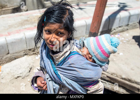 Una bambina porta un piccolo bambino sulla schiena. Bambini di strada che pregano di turisti per le strade di Leh in Ladakh. India luglio 2015 Foto Stock