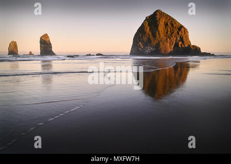 Haystack Rock Sunrise, Cannon Beach, Oregon Sunrise a Haystack Rock in Cannon Beach, Oregon, come il surf lavaggi fino sulla spiaggia. Stati Uniti. Foto Stock