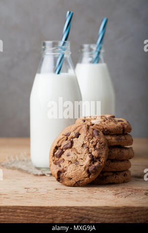 Una pila di biscotti con cioccolato al latte e due bottiglie di latte su un tavolo di legno. Foto Stock