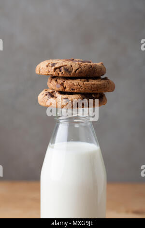 Bottiglia con latte e biscotti con scaglie di cioccolato su sfondo scuro. Foto Stock