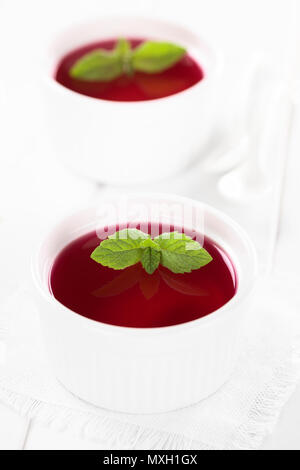 Gelatina rossa o jella in bianco ciotole guarnite con foglie di menta (messa a fuoco selettiva, concentrarsi sulle punte delle foglie di menta nel primo recipiente) Foto Stock