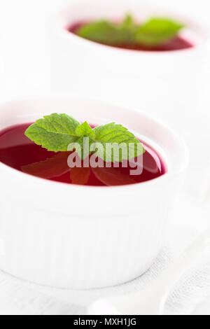 Gelatina rossa o jella in bianco ciotole guarnite con foglie di menta (messa a fuoco selettiva, concentrarsi sulle punte delle foglie di menta nel primo recipiente) Foto Stock