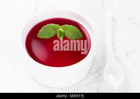 Gelatina rossa o jella nella ciotola bianco guarnito con foglie di menta (fuoco selettivo, la messa a fuoco su grandi foglie di menta) Foto Stock