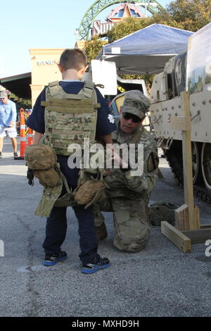 Un U.S. Soldato con la prima divisione di cavalleria fuori di Ft. Cappa, Tx. consente di montare l'ingranaggio di combattimento su un giovane bambino all'l'Accademia Militare degli Stati Uniti a West Point contro l'Università di Notre Dame del gioco del calcio al Alamodome a San Antonio nov. 12 2016. La prima divisione di cavalleria aveva una mostra al di fuori dell'Alamodome a promuovere esercito-legami civili. (U.S. La riserva di esercito foto di Spc. Ian Valley 345 PAD/rilasciato) Foto Stock