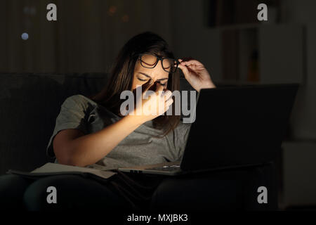 Stanco donna sofferenza affaticamento degli occhi che studiano nella notte con un portatile a casa Foto Stock