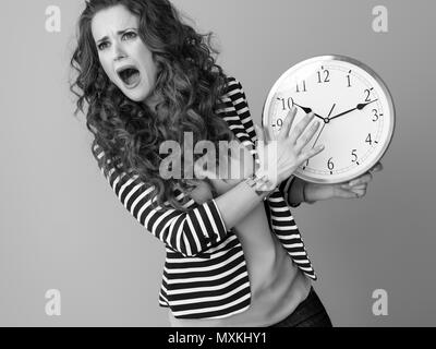 Triste donna elegante in camicia a righe sullo sfondo con orologio Foto Stock