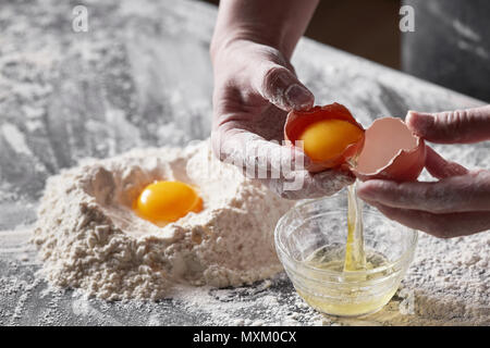 Mani femminili tenere un uovo rotto nelle mani di un tavolo da cucina. Concetto di cottura Foto Stock