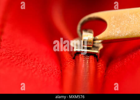 Zipper aprire parzialmente il legame tra due strati di tessuto rosso di prodotti tessili e di cuoio rosso sotto un elevato ingrandimento vicino dettaglio. Foto con profondità o Foto Stock