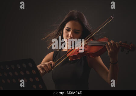 Piuttosto giovane donna riproduzione di un violino su sfondo nero. Foto Stock