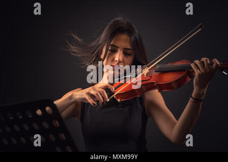 Piuttosto giovane donna riproduzione di un violino su sfondo nero. Foto Stock