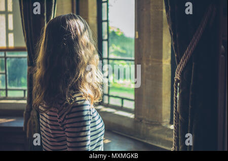 Una giovane donna è guardando fuori dalla finestra di una casa in campagna Foto Stock