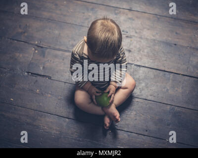 Un piccolo bambino è seduta sul parquet con un Apple Foto Stock