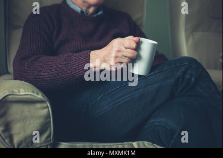 Un anziano uomo è in un momento di relax a casa con una tazza di tè Foto Stock
