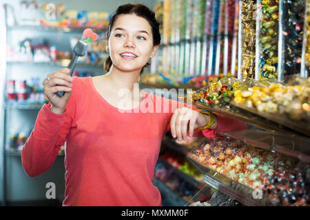 La ragazza è felice di prendere in considerazione i diversi tipi di caramelle in negozio Foto Stock