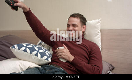 Giovane uomo guardare la TV a letto e bere il tè Foto Stock