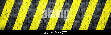 Vecchio e stagionato grungy muro di mattoni con pericolo o attenzione nero e giallo di avvertimento di strisce diagonali come sfondo di texture in ampio panorama banner f Foto Stock