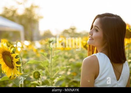 Vista di profilo di giovani felici donna asiatica sorridente e pensare in Foto Stock