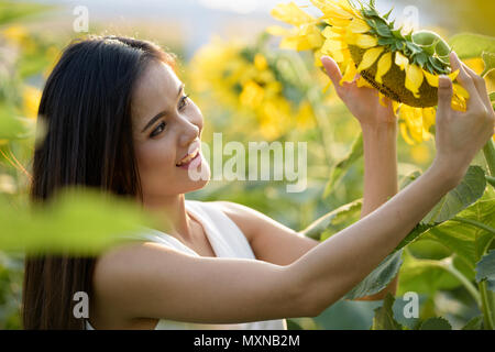 Felice giovane donna asiatica sorridente e guardando il girasole in Foto Stock