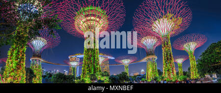 Singapore - Aprile 29, 2018: panorama di Supertree Grove con ponte sopraelevato a giardini dalla baia illuminato in blu ora e Marina Bay Sands in area di Marina Bay. Popolare attrazione turistica di Singapore. Foto Stock