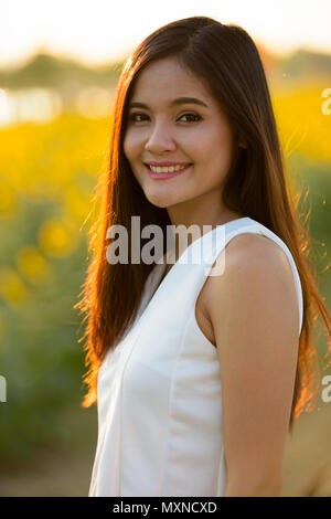 Felice giovane donna asiatica sorridente contro il campo della fioritura sunflo Foto Stock