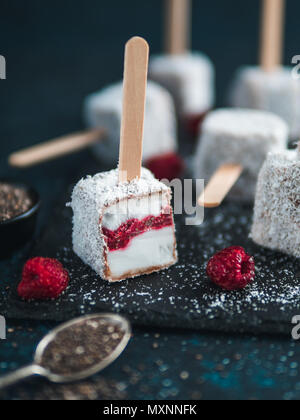 In casa materie lamington gelato pop su sfondo scuro. Australian dessert lamington con chia e confettura di lamponi, cioccolato e cacao cappotto. Cibo Vegan ricetta e idea. Copia spazio per il testo Foto Stock