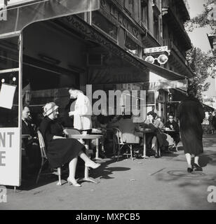 Degli anni Cinquanta, storico, un cameriere che serve i parigini seduto fuori un cafè sul marciapiede in Parigi, Francia. Foto Stock