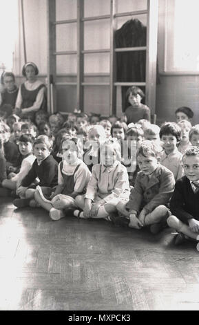 1964, storico gruppo di bambini della scuola primaria seduti insieme all'interno sul pavimento per il montaggio, Inghilterra, Regno Unito. Foto Stock