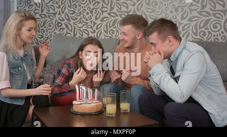 Attraente ragazza teen festeggia il suo compleanno con gli amici a casa e si brucia le candeline sulla torta e bevande juce arancione Foto Stock