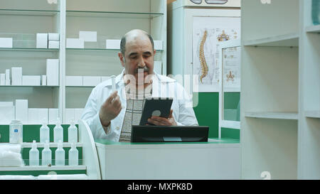 Senior farmacista avente la video chat con client utilizzando un tablet pc in drug store Foto Stock