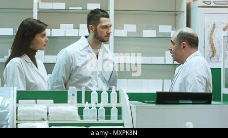 Anziani al farmacista e gli assistenti di parlare seriamente in farmacia reception Foto Stock