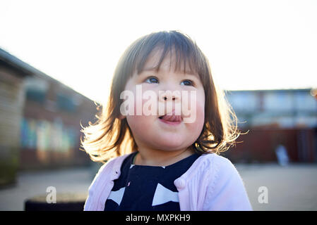 Ritratto di un simpatico giovani asiatici bambina con le guance rosey in tempo freddo fuori la sua lingua Foto Stock