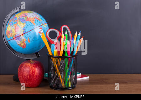 Accessori per la scuola e un Apple su un desktop con una lavagna sfondo per lo spazio di copia Foto Stock