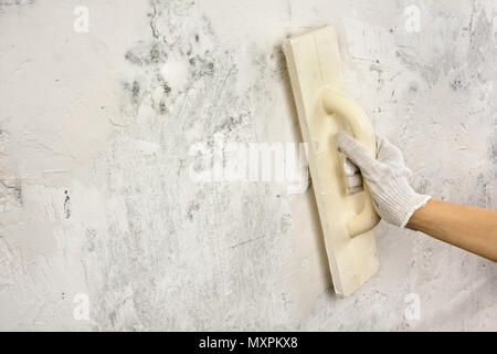 Intonaci a mano e lisciatura della parete di calcestruzzo con cazzuola durante la riparazione Foto Stock