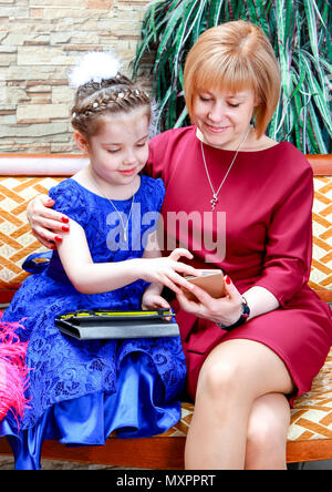 Elegante madre e figlia in Studio. Mom mostra qualcosa sul suo telefono a sua figlia. Foto Stock