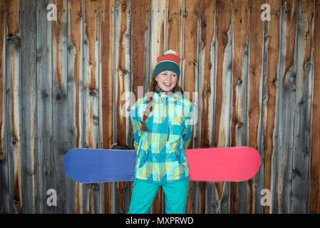 Bella Snowboarder ragazza in un costume verde in appoggio sulla terrazza di una casa in legno in montagna Foto Stock