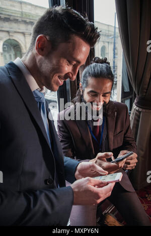 Vista laterale di due imprenditori sui loro telefoni intelligenti di sostituzione dettagli contatto. Entrambi a sorridere e ridere. Foto Stock