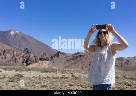 Donna di scattare una foto sul suo telefono cellulare con un vulcano in background Foto Stock