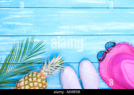 Blu sullo sfondo di legno, calzature, ananas, rosa hat, ramo di palma, occhiali da sole e posto per il testo al centro. Accessori per la spiaggia e le vacanze. Cop Foto Stock