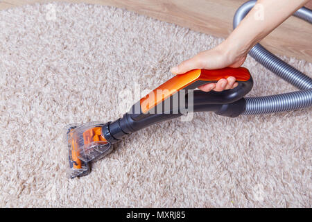 Persona di raccolto utilizzando palmare aspirapolvere a casa e il lavaggio morbida moquette sul pavimento in legno. Foto Stock