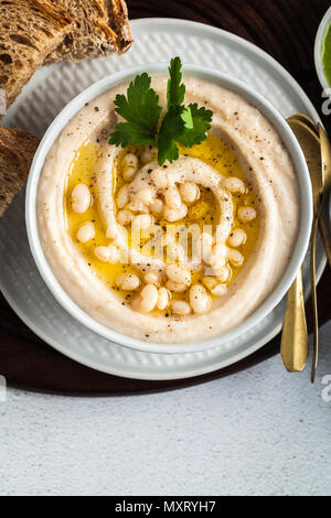 Hummus di bianco fagioli cannellini, serviti con pesto di rucola e pane di segale, olive e limone su un tavolo Foto Stock