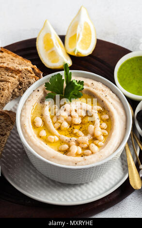 Hummus di bianco fagioli cannellini, serviti con pesto di rucola e pane di segale, olive e limone su un tavolo Foto Stock