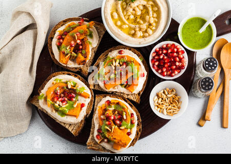 Snack vari tipi di pane con hummus e zucca cotta su una scheda che serve con pesto di rucola. i semi di melograno e pinoli. cibo sano Foto Stock