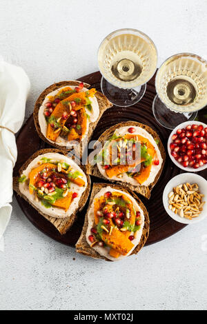 Snack vari tipi di pane con hummus e zucca cotta su una scheda che serve con pesto di rucola. i semi di melograno e pinoli. cibo sano e vino bianco Foto Stock