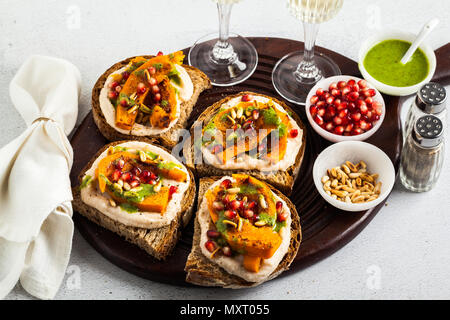 Snack vari tipi di pane con hummus e zucca cotta su una scheda che serve con pesto di rucola. i semi di melograno e pinoli. cibo sano e vino bianco Foto Stock